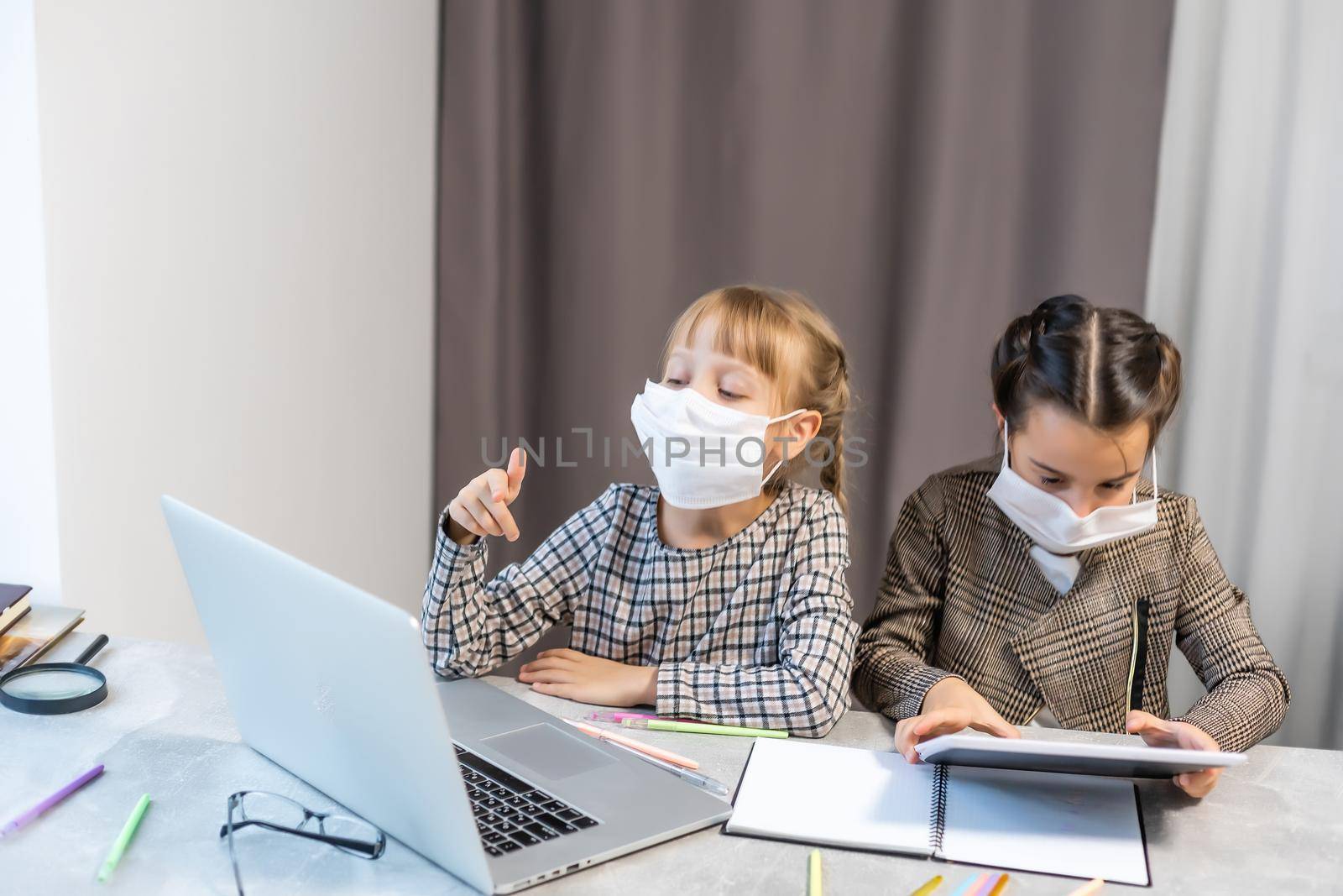 Young elementary school girls with face protective mask watching online education class. Coronavirus or Covid-19 lockdown education concept. by Andelov13