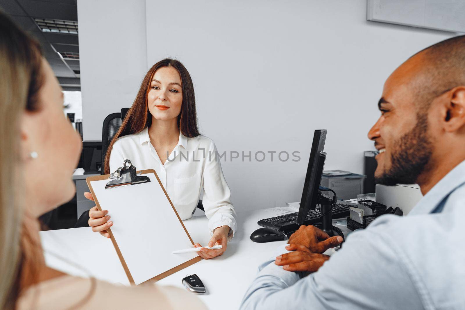 Young woman car seller showing contract to couple of car buyers in her office
