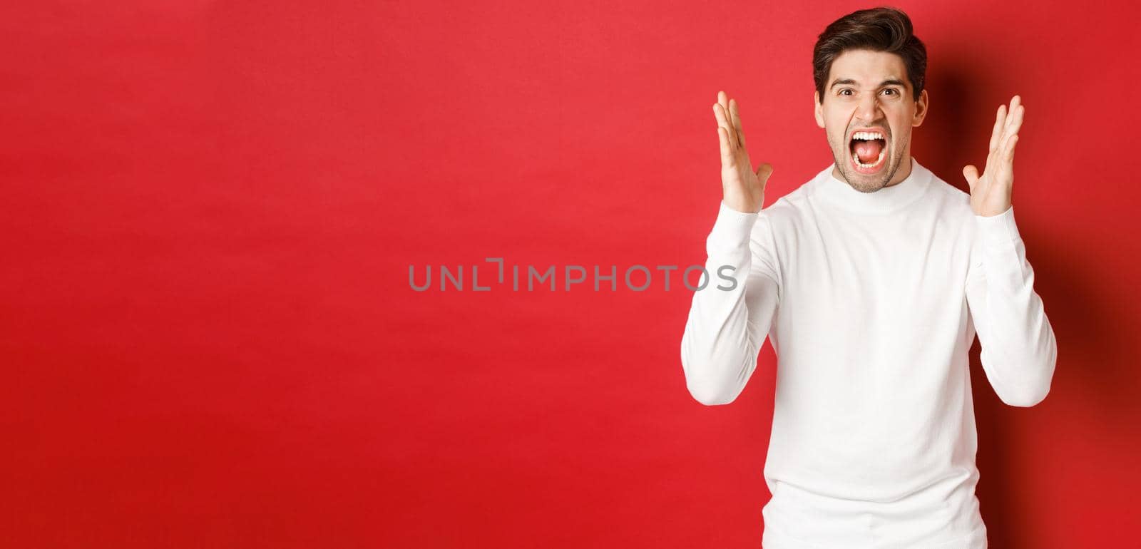 Image of frustrated and angry man in white sweater, shouting in rage, being mad at someone, standing over red background by Benzoix