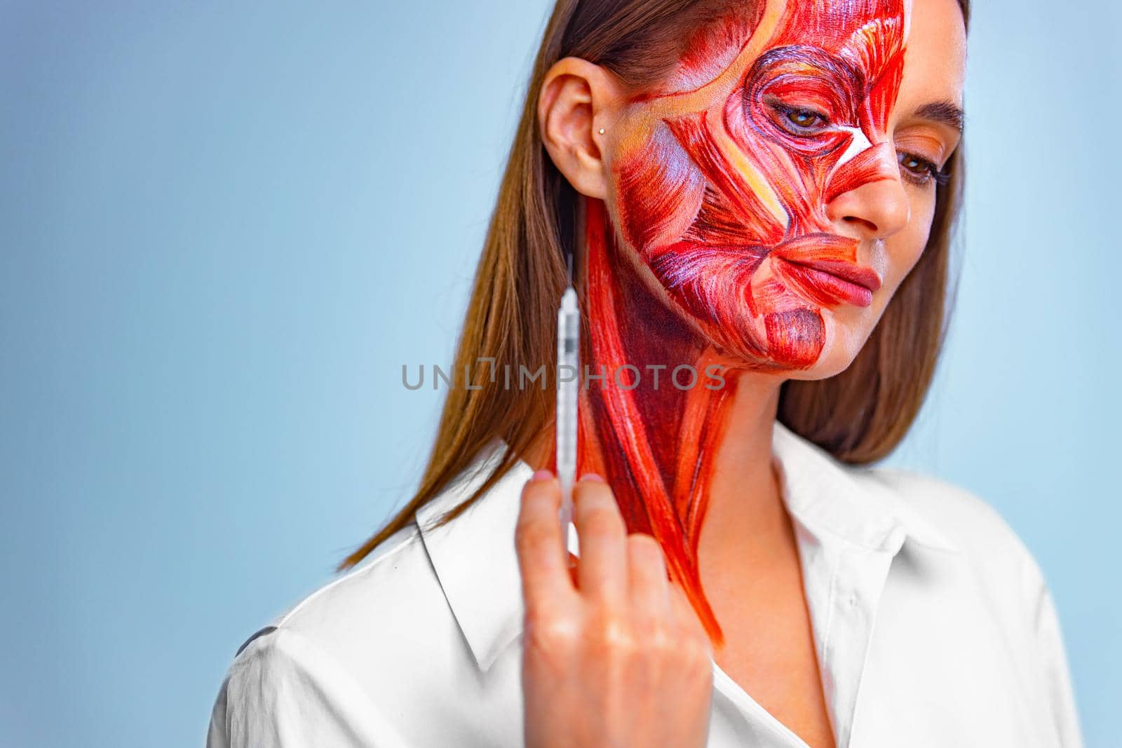 Cosmetic injection in the face. Young woman with half of face with muscles structure under skin. Model for medical training on a light background. by MikeOrlov