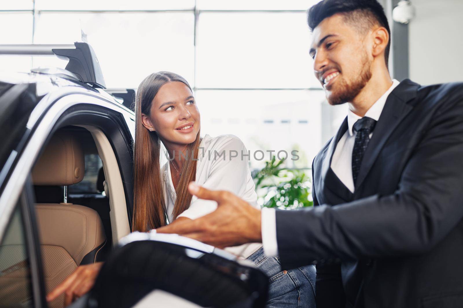 Young attractive woman looking for a new car in a showroom by Fabrikasimf