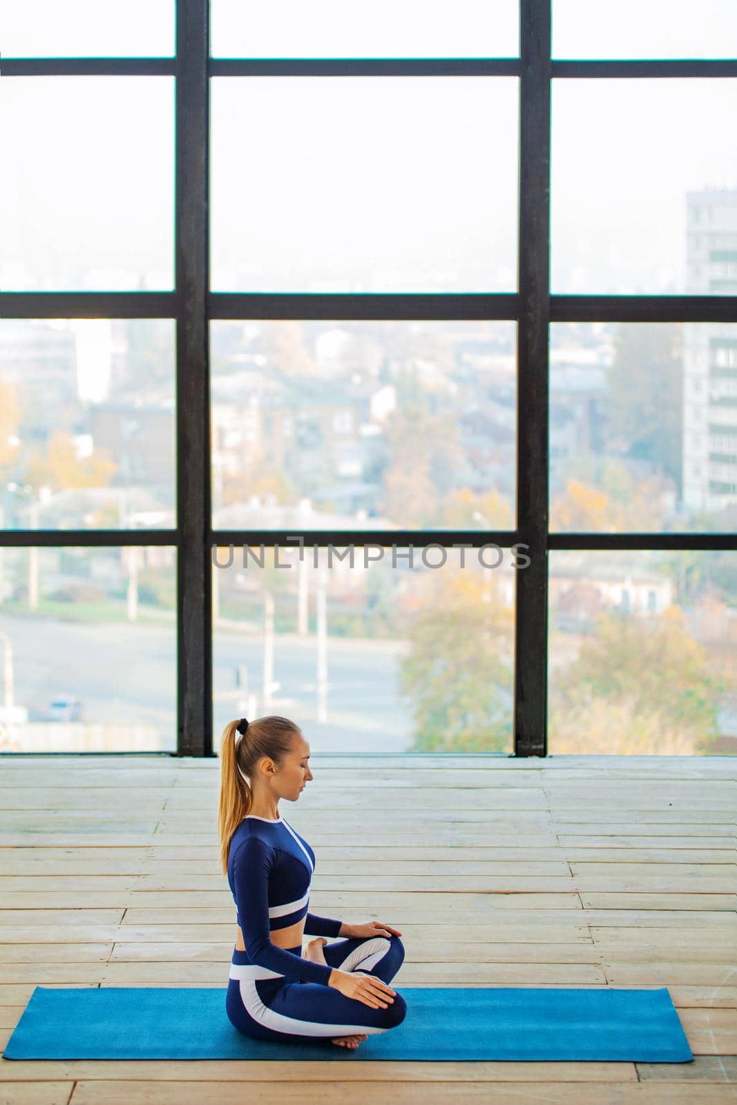 Yoga asana Indoor before a large panoramic window. Sports recreation. Beautiful young woman in yoga pose. Individual sports. by MikeOrlov