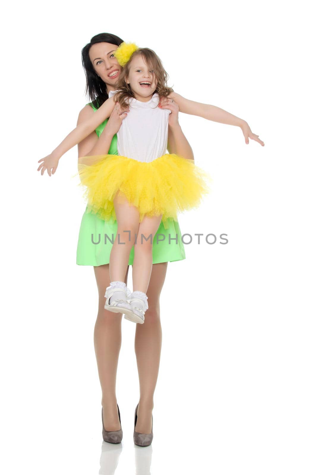 Beautiful young mother in a short green dress and her little beloved daughter in a yellow skirt.Fun mother throws daughter on hands.Isolated on white background.