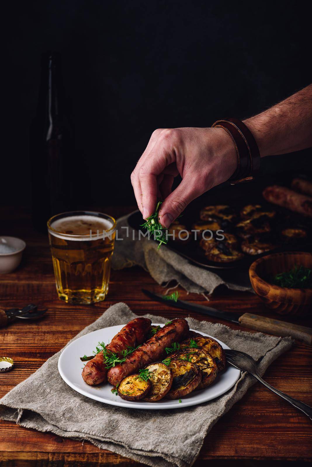 Pork Sausages Baked with Eggplant and Herbs on White Plate. Man Garnishing Meal with Dill