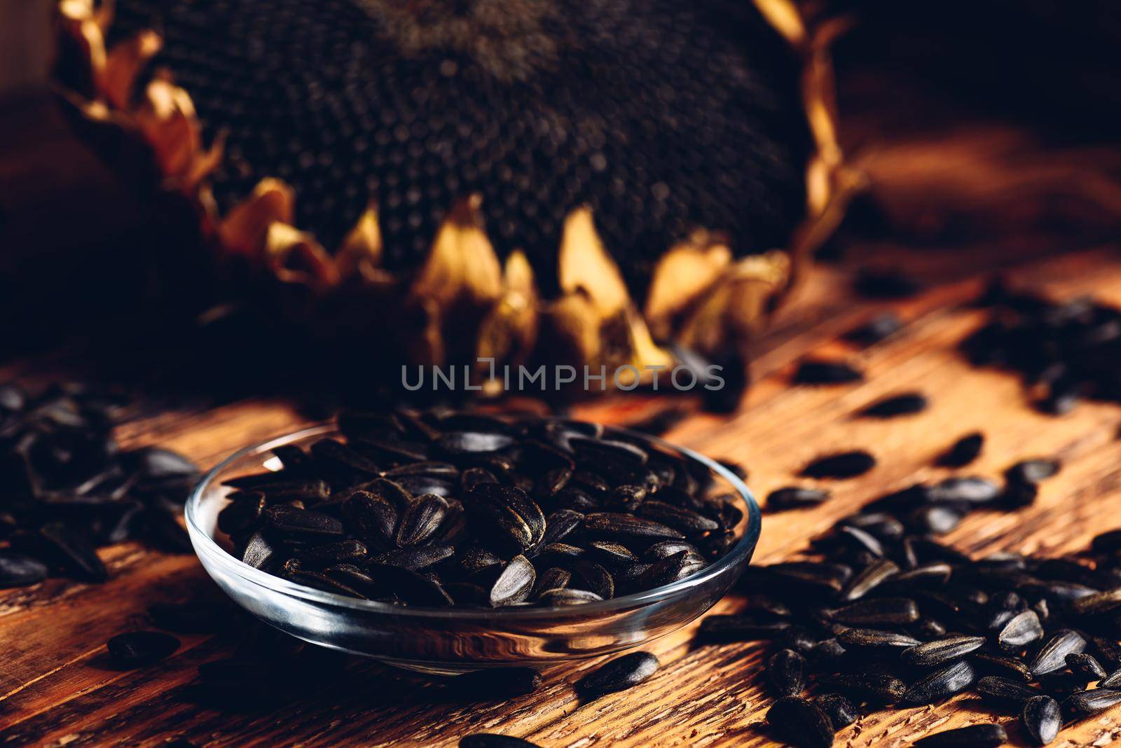 Roasted seeds on the glass saucer and dried sunflower over old wooden surface