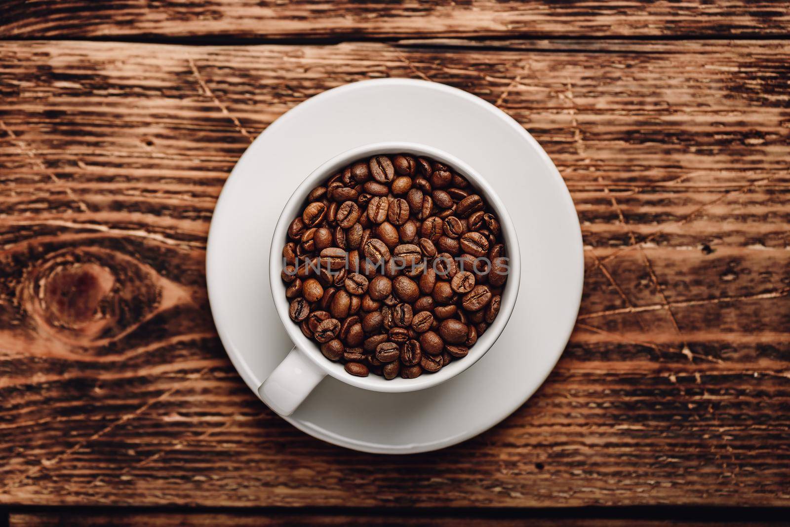 Roasted coffee beans in cup over wooden surface