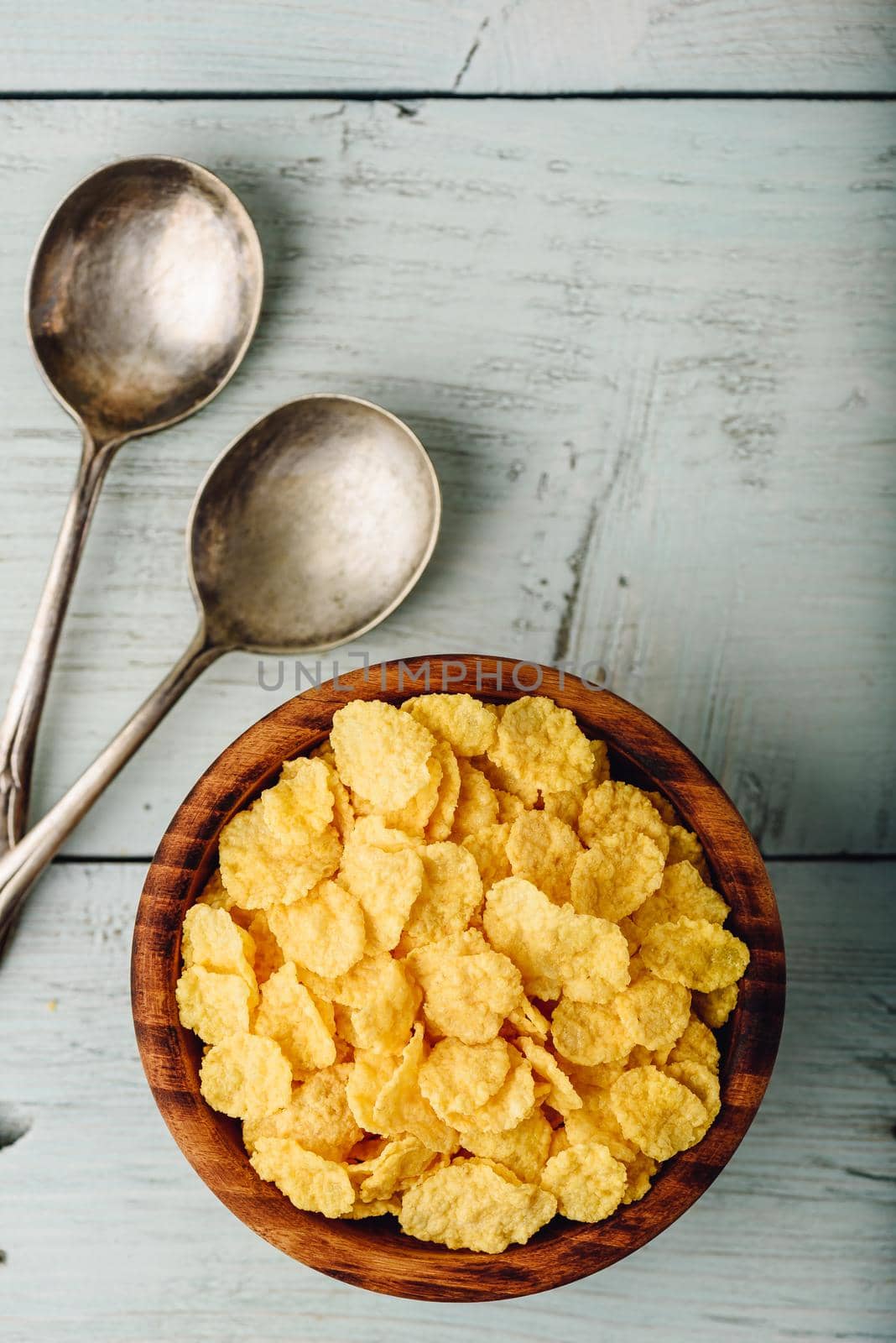 Rustic bowl of corn flakes with spoons on a wooden surface