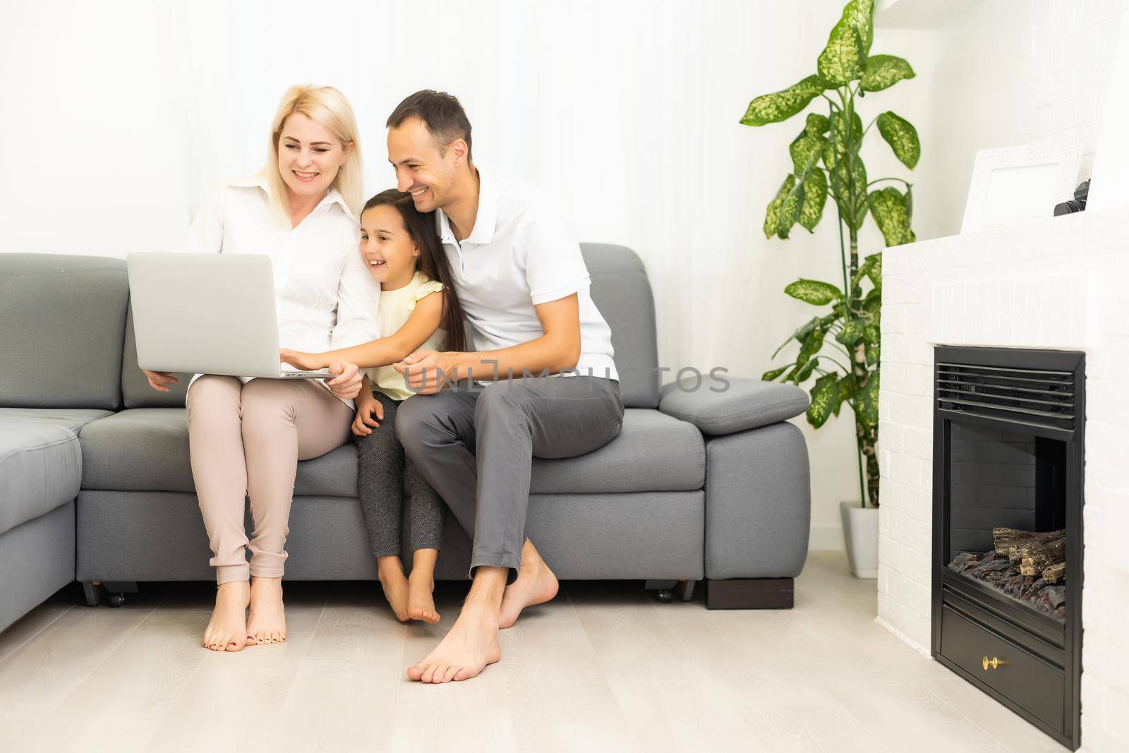 Happy family with kid girl having fun using laptop together sitting on sofa, parents and child daughter laughing relaxing at home with computer watching funny internet video, making online call by Andelov13