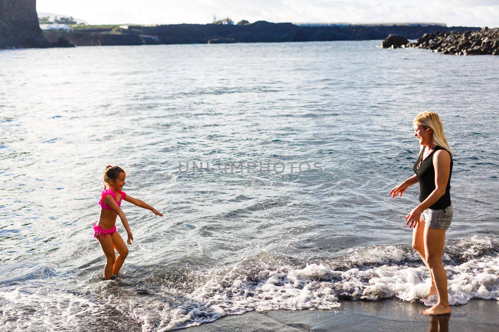 Family holiday on Tenerife, Spain. Mother with daughter outdoors on ocean. Portrait travel tourists - mom with daughter. Positive human emotions, active lifestyles. Happy young family on sea beach by Andelov13