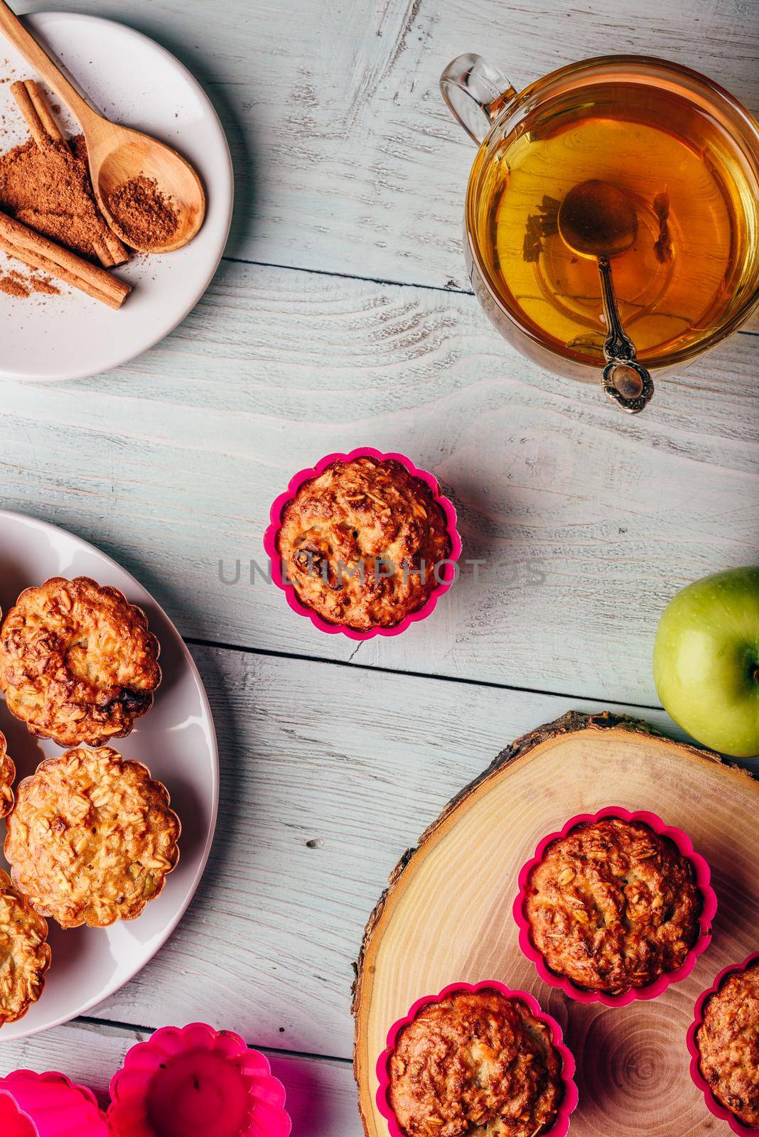 Healthy Breakfast. Cooked oatmeal muffins with apple and cup of green tea over light wooden background. View from above.
