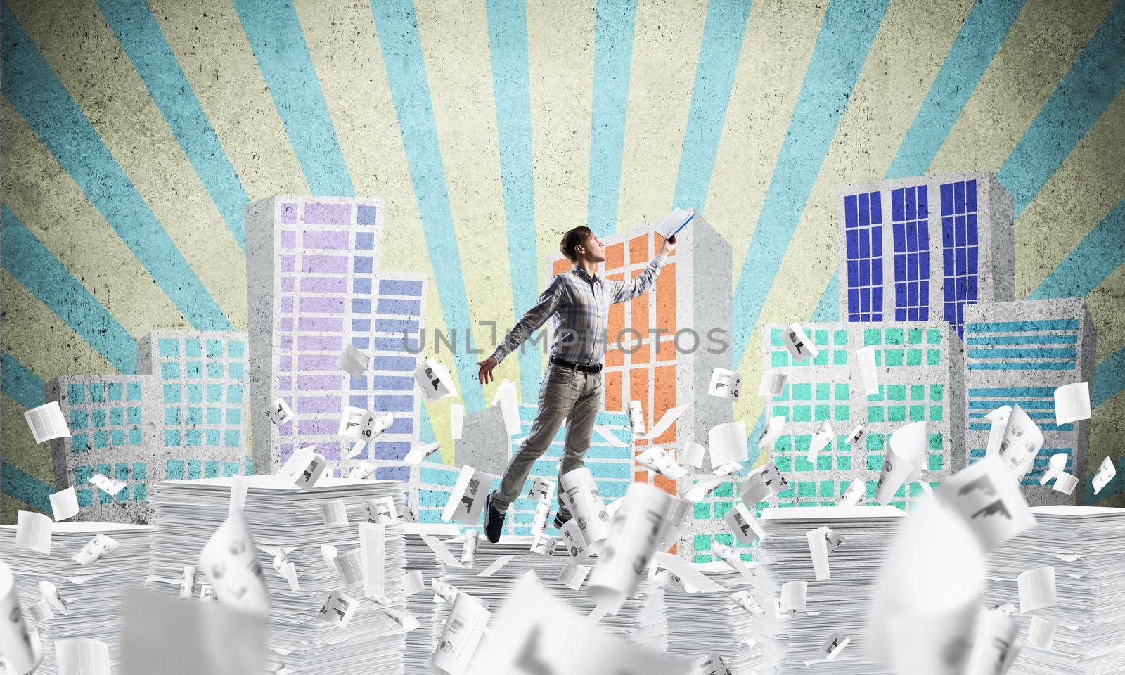 Man in casual wear keeping hand with book up while standing among flying papers with drawn cityscape on background. Mixed media.