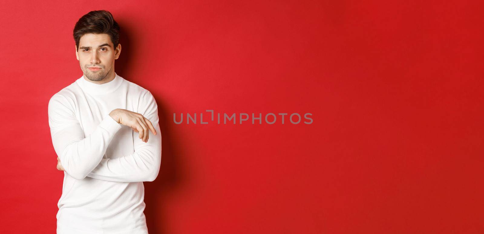 Image of sassy caucasian man in white sweater, looking thoughtful at camera, making choice, standing over red background by Benzoix