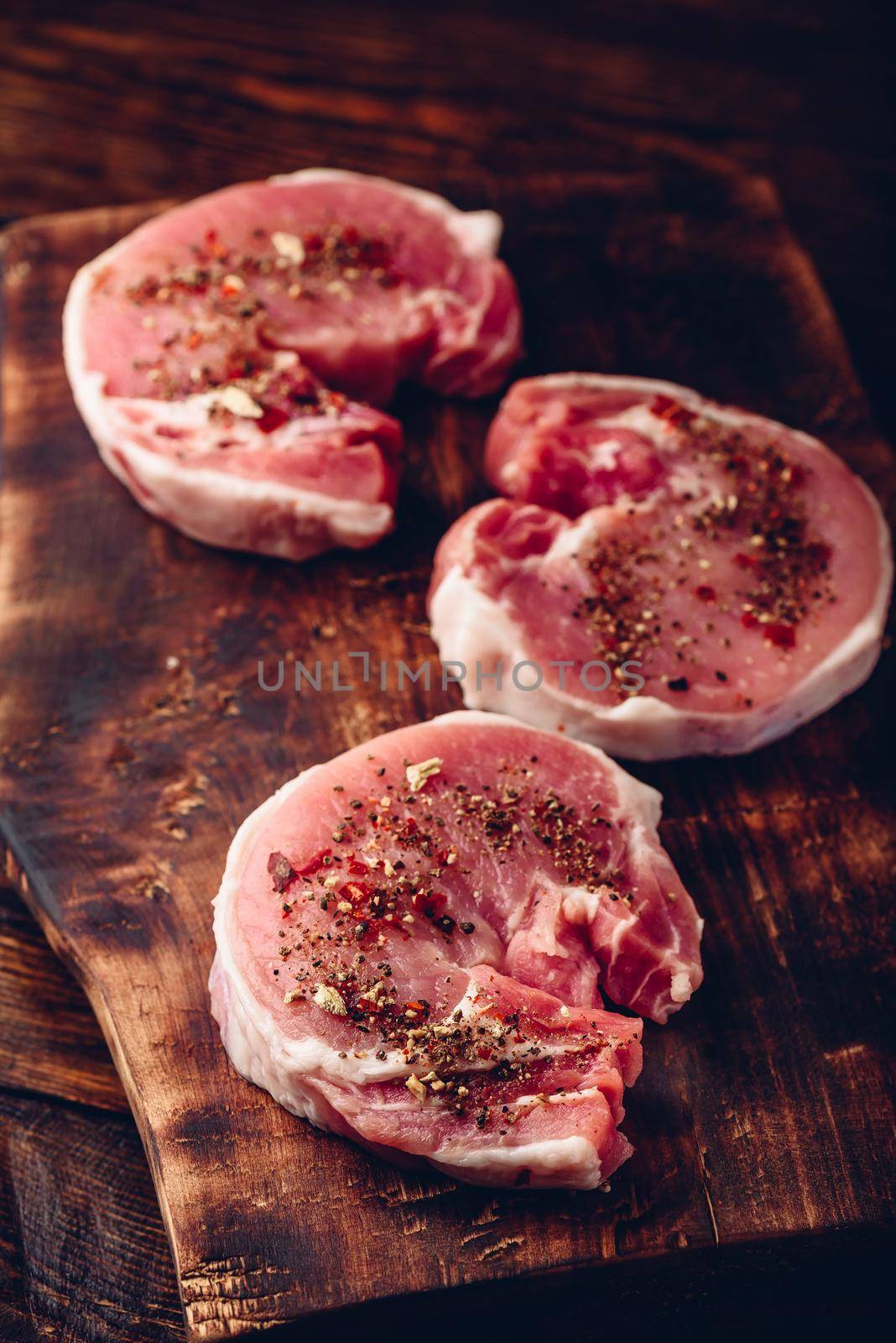 Raw pork loin steaks with different spices on rustic cutting board