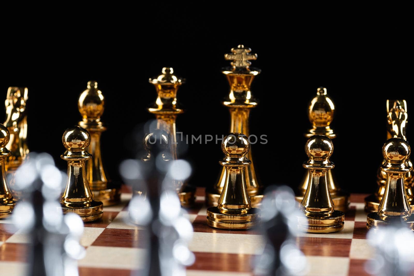 Gold and silver chess figures standing on chessboard. Intellectual and tactic game. Strategy planning, leadership and teamwork business concept. Close-up metal chess pieces on black background.