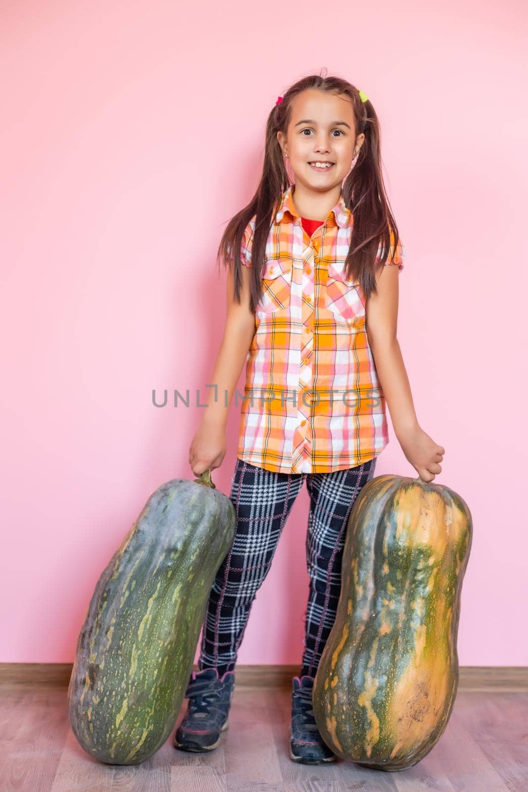 Picture of cheerful positive little girl with pumpkin over pink wall background holding pumpkin showing peace. by Andelov13