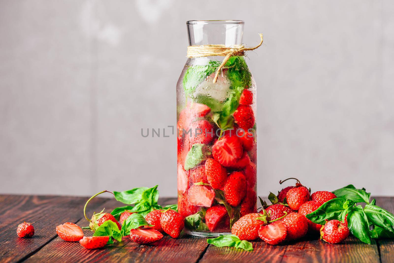 Bottle of Detox Water Infused with Fresh Strawberry and Basil Leaves. Scattered Ingredients on Wooden Table. Copy Space.