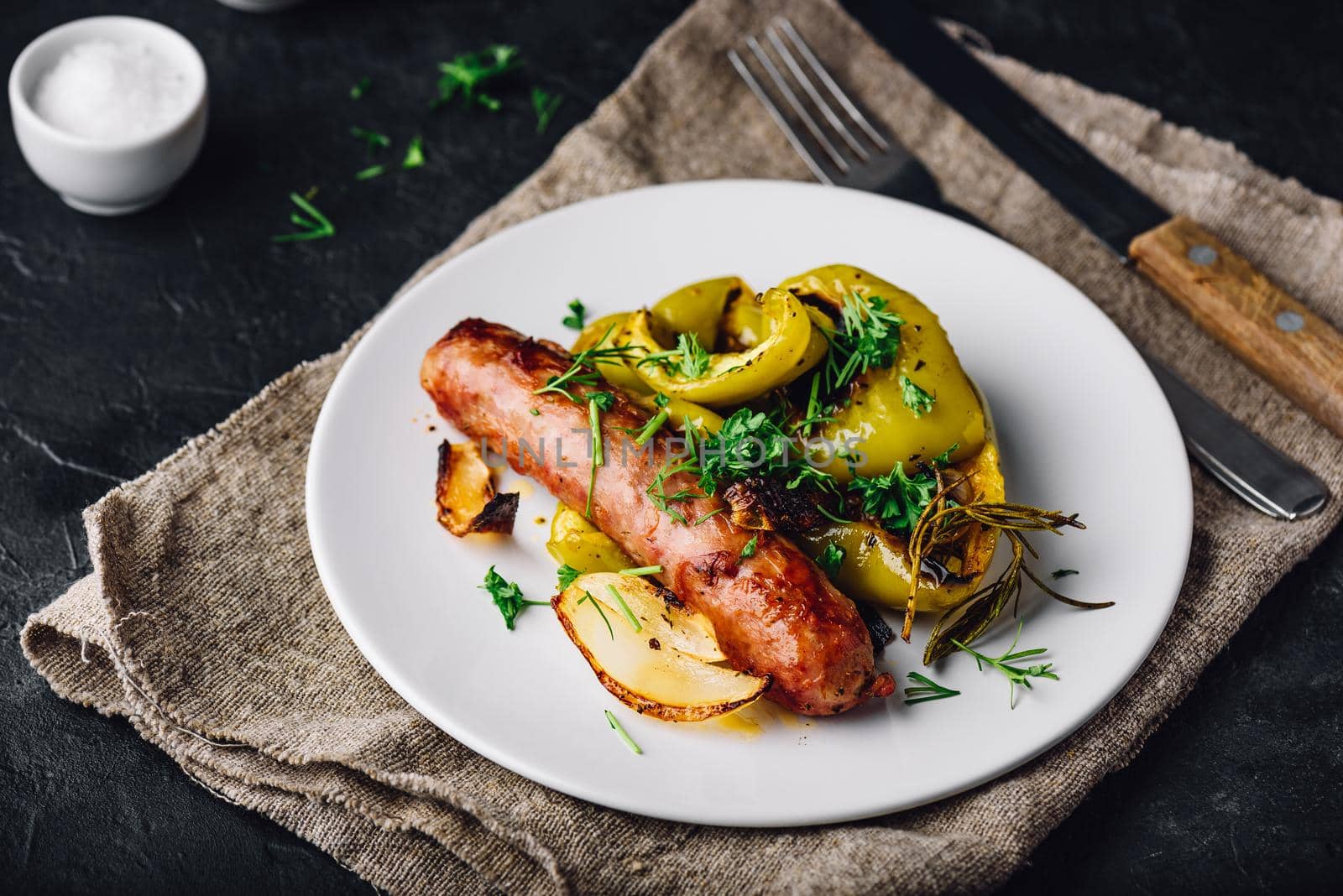 Pork sausage baked with bell peppers, onions and different herbs on white plate