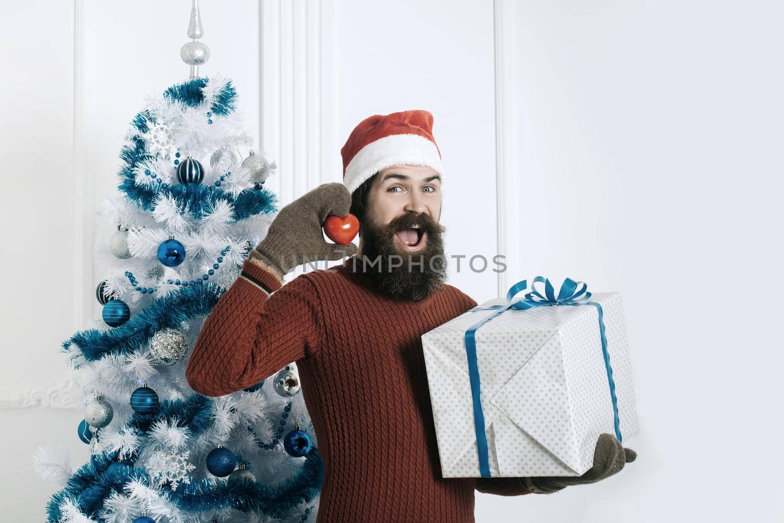 Santa claus man with heart toy and gift. New year guy at blue Christmas tree. Winter holiday and xmas. Christmas man with beard on happy face at present box.