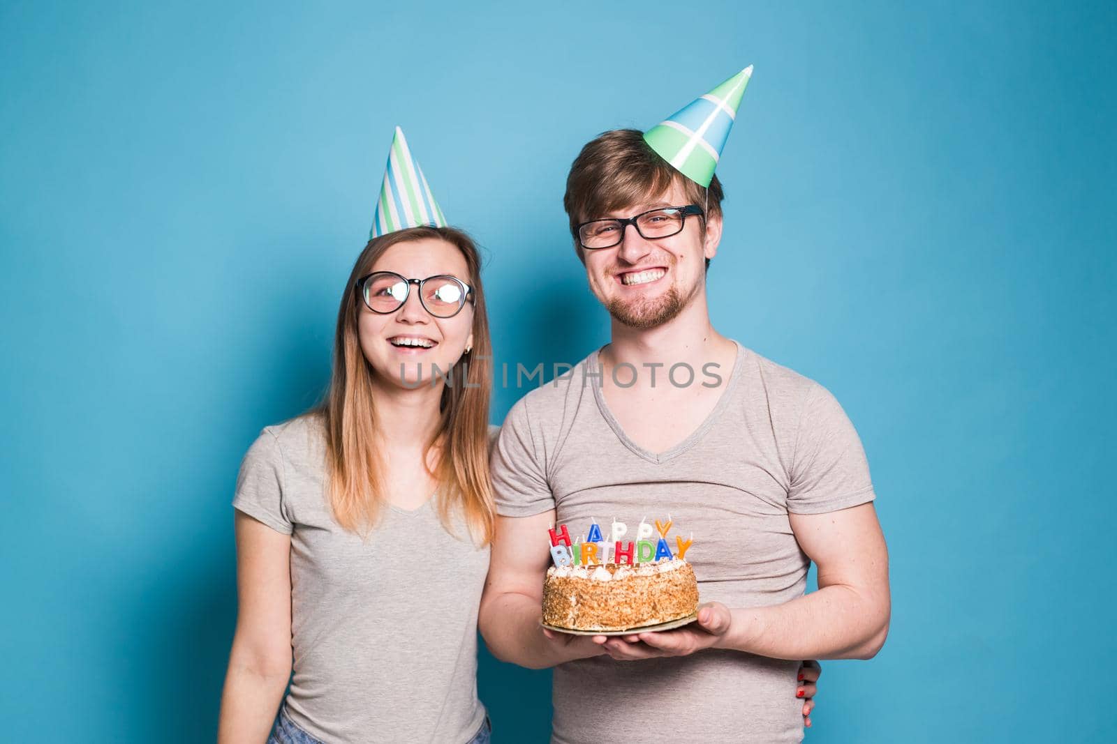 Young cheerful students charming girl and nice guy in greeting paper caps holding a cake with a bengal sparks candle. Concept of congratulations on the holiday and anniversary
