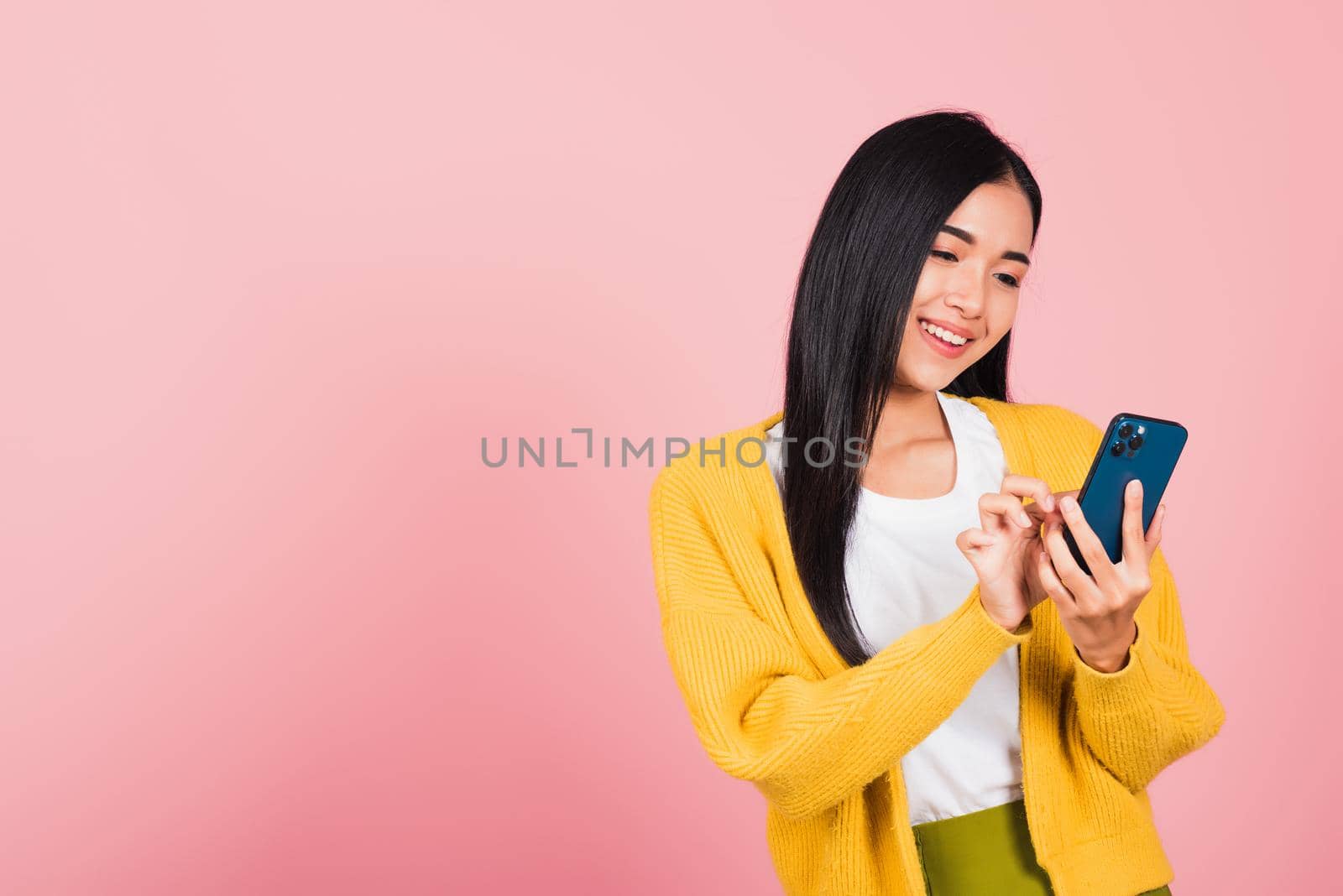 Happy Asian portrait beautiful cute young woman teen smiling excited typing text message on smart mobile phone enjoys online communication isolated, studio shot on pink background with copy space