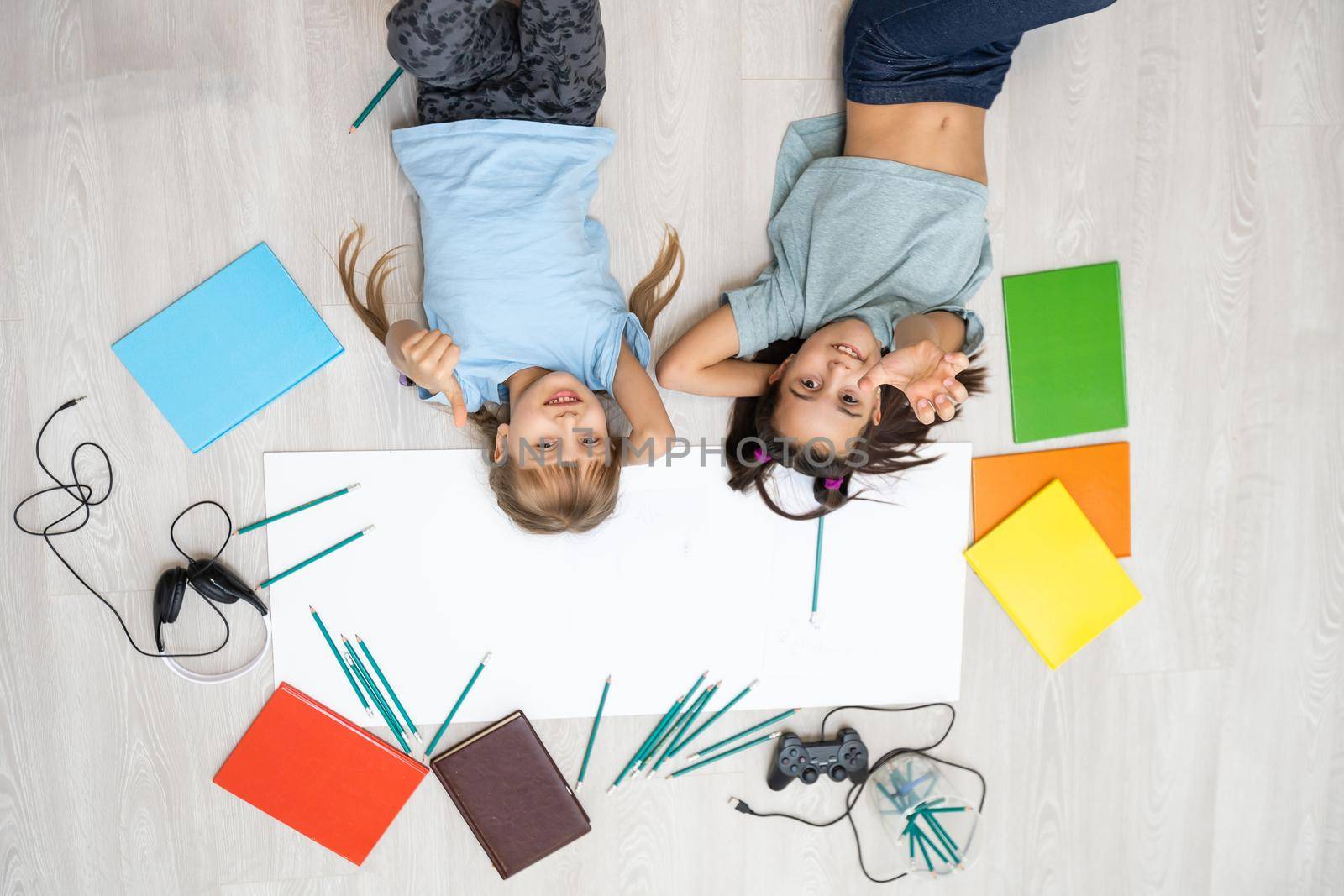 two little girls sisters lie on the floor of the house and draw with colored pencils on paper. children do creative homework after school. by Andelov13