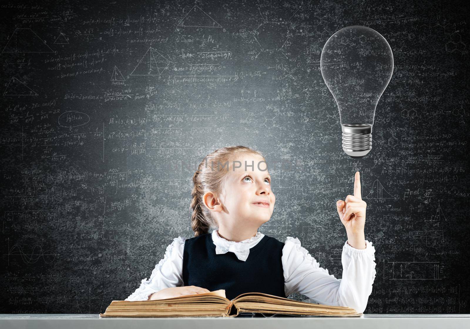 Little girl scientist with microscope on chalkboard background with light bulb. Research and discovery concept. Elementary science class in modern school. Schoolgirl in schoolwear sitting at desk