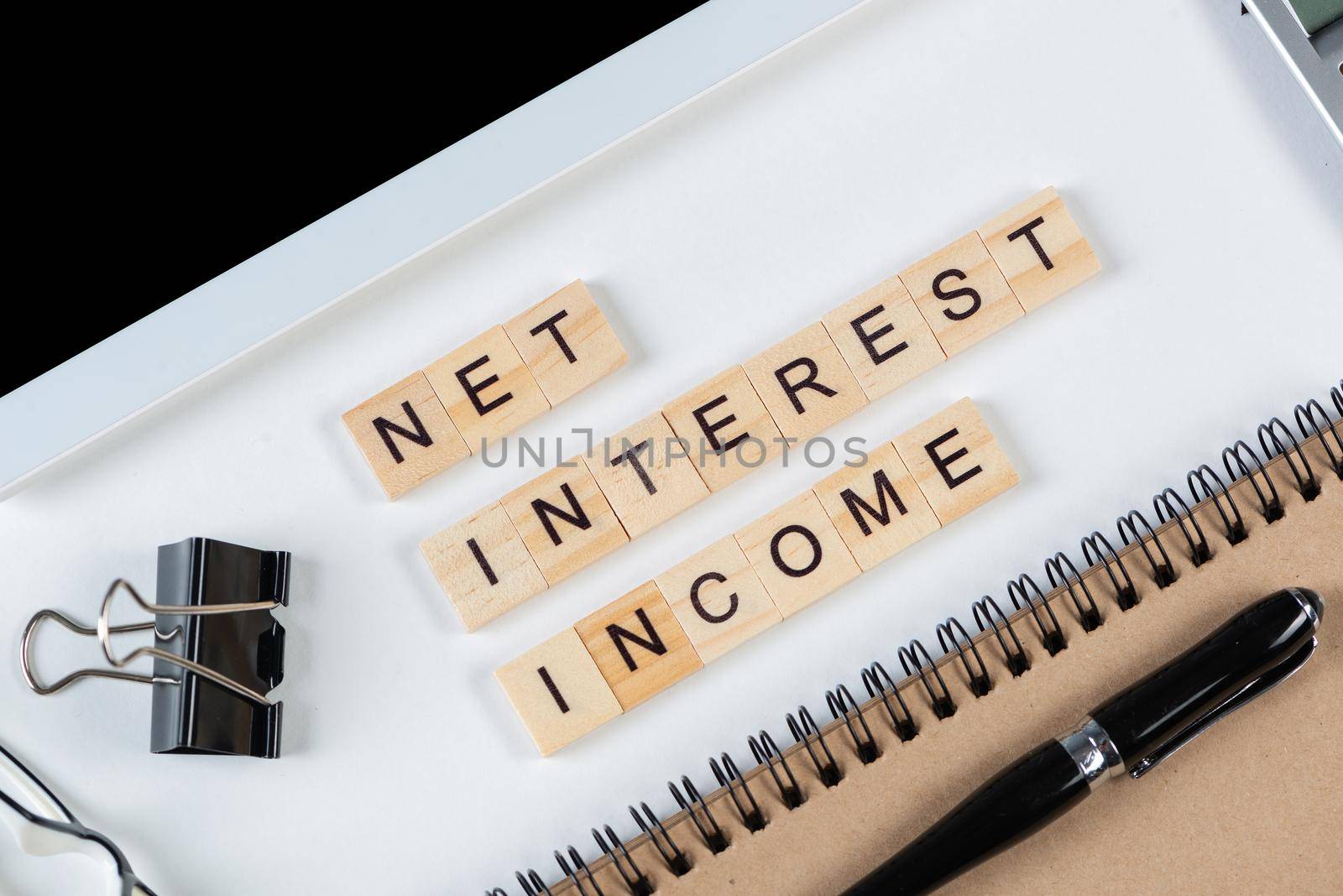 Net interest income concept with letters on wooden cubes. Still life of office workplace with supplies. Flat lay white surface with tablet computer and notepad. Financial management and accounting