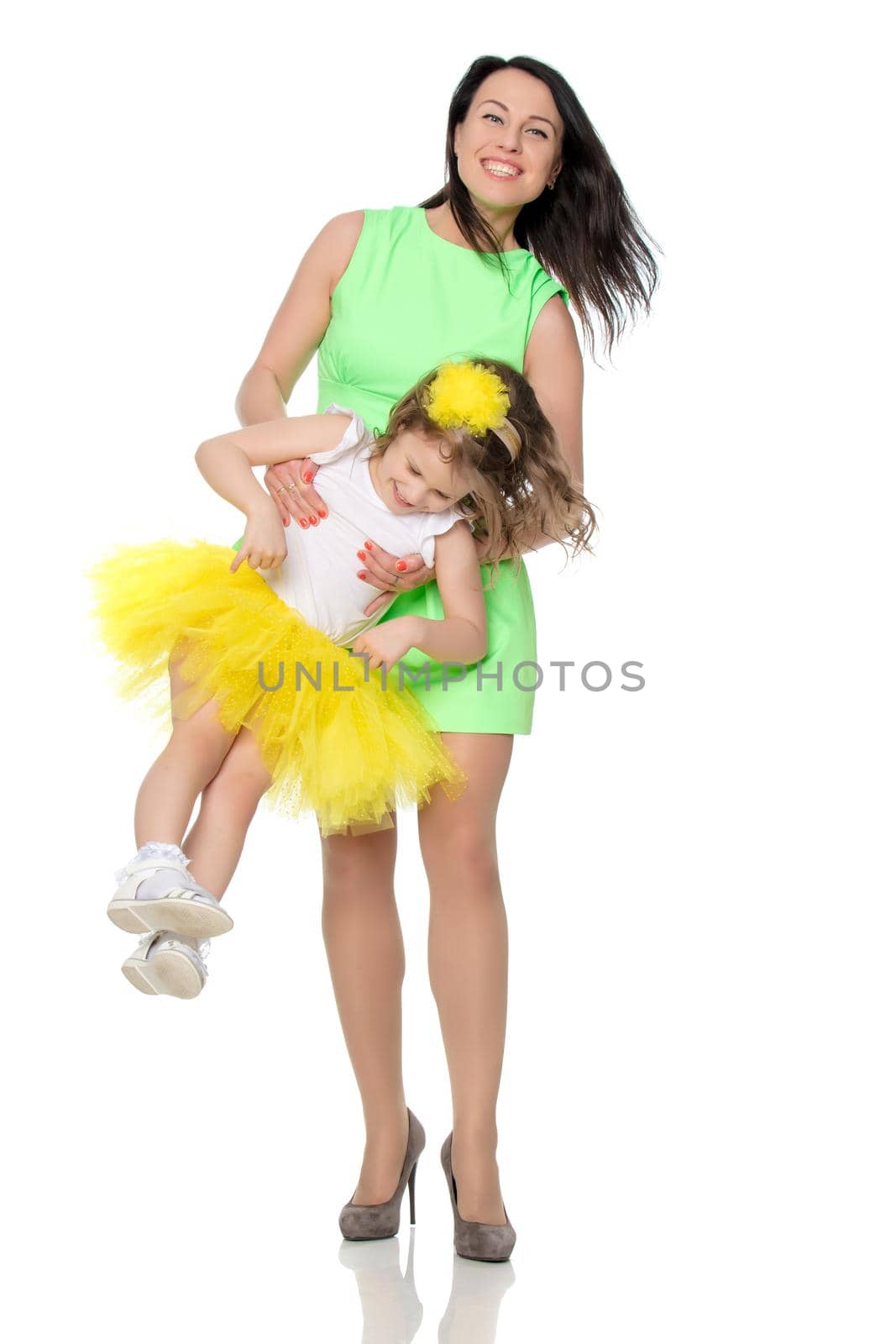 Beautiful young mother in a short green dress raises hands his precious baby daughter.Isolated on white background.