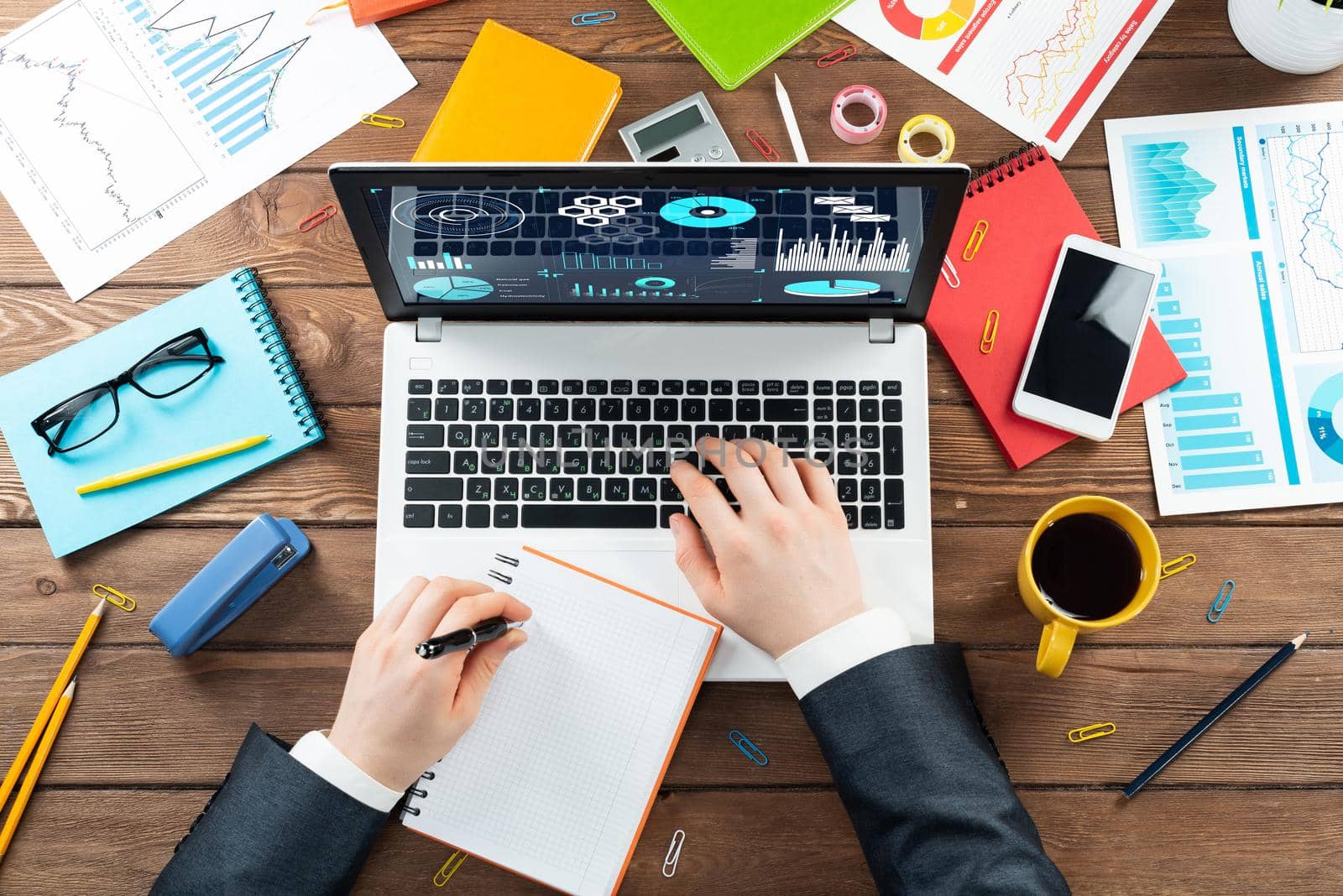 Close up business analyst working at laptop. Top view office workplace with computer and financial documents. Business occupation design with man in business suit sitting at vintage wooden desk.