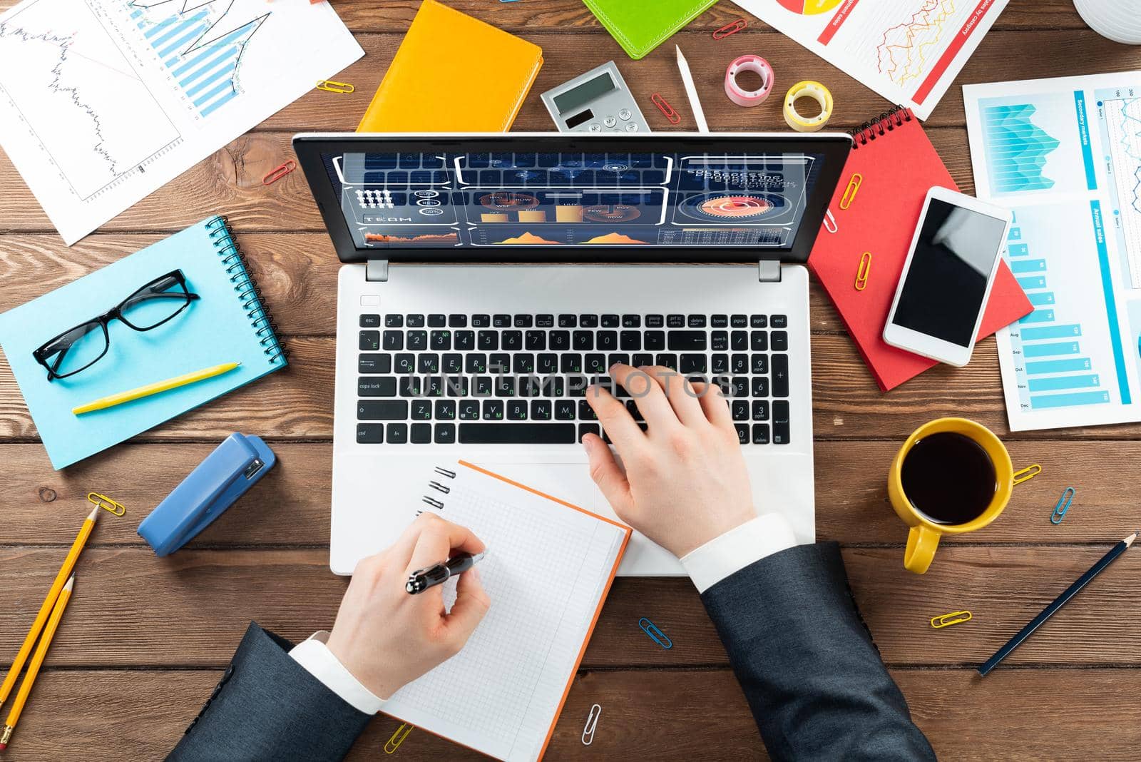 Close up businessman hands working at laptop. Top view office workplace with computer and financial documents on wooden table. Business occupation design with man in business suit sitting at desk