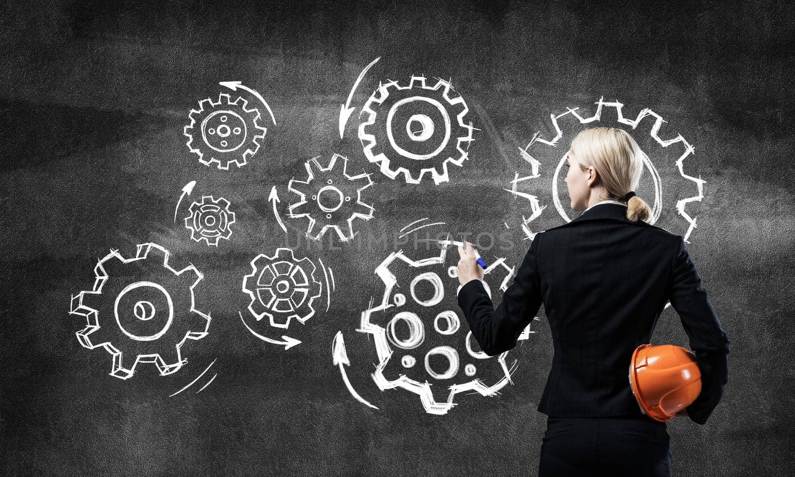 Businesswoman draws cogwheel mechanism on chalkboard. Woman in business suit with safety helmet. Mechanical system engineering and project management. Business solution planning and designing.