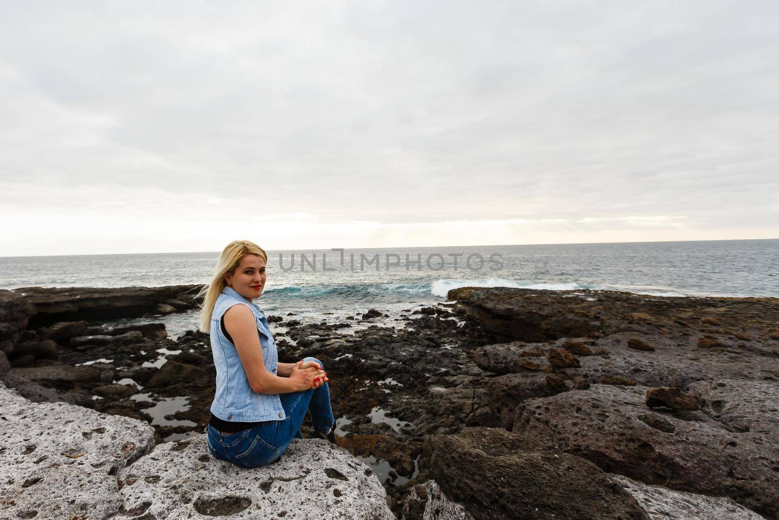 Women on volcanic rocks and blue ocean with waves, white foam and volcanic rocks. Canary Islands. The magnificent coast of the Atlantic Ocean.