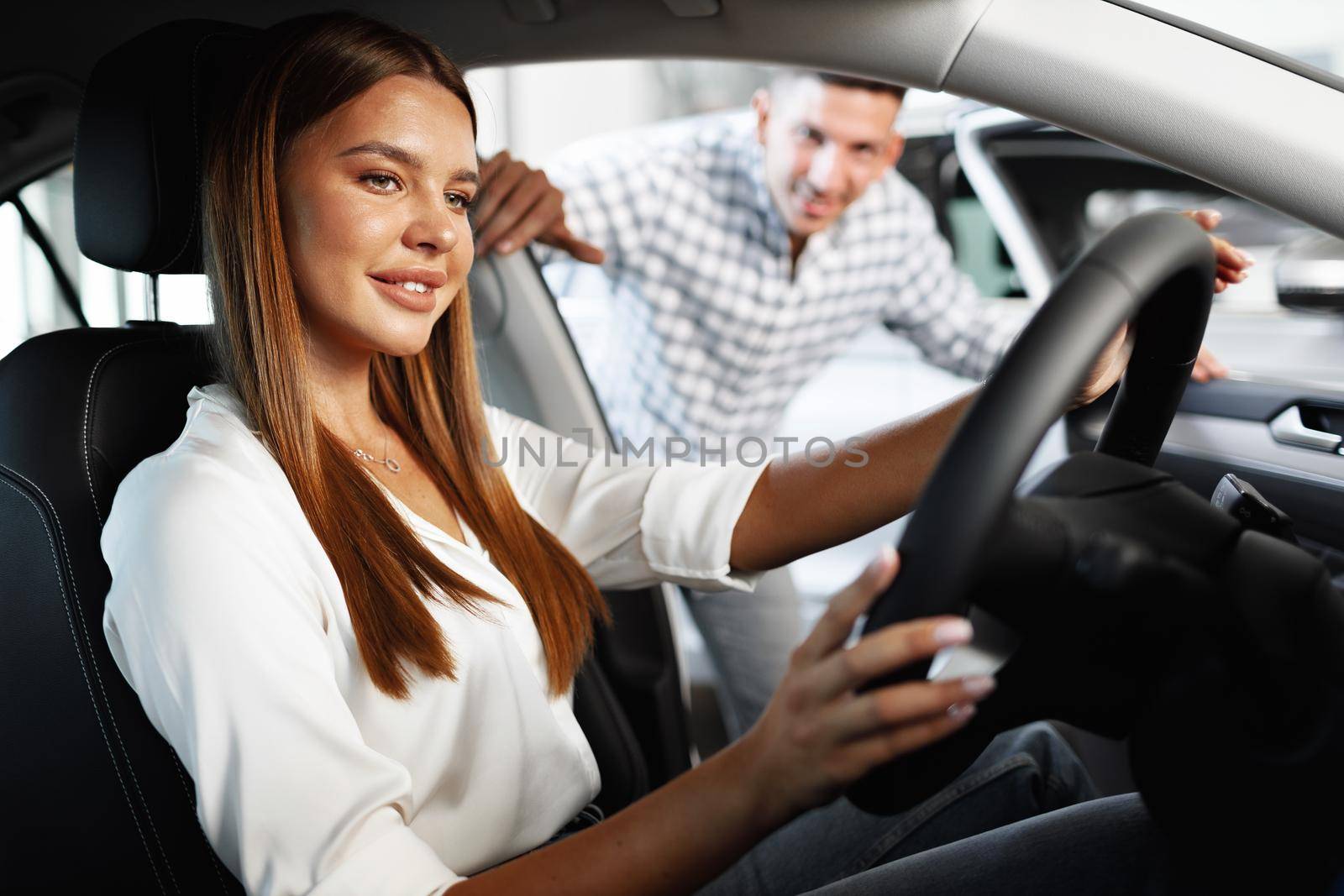 Young attractive woman looking for a new car in a car showroom