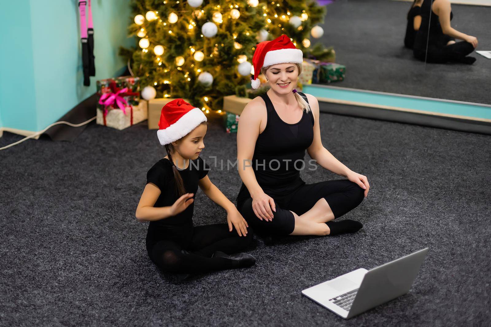 Mother and daughter practicing online yoga lesson at home at quarantine isolation period during coronavirus pandemic. Family doing sport together online from home. Healthy lifestyle