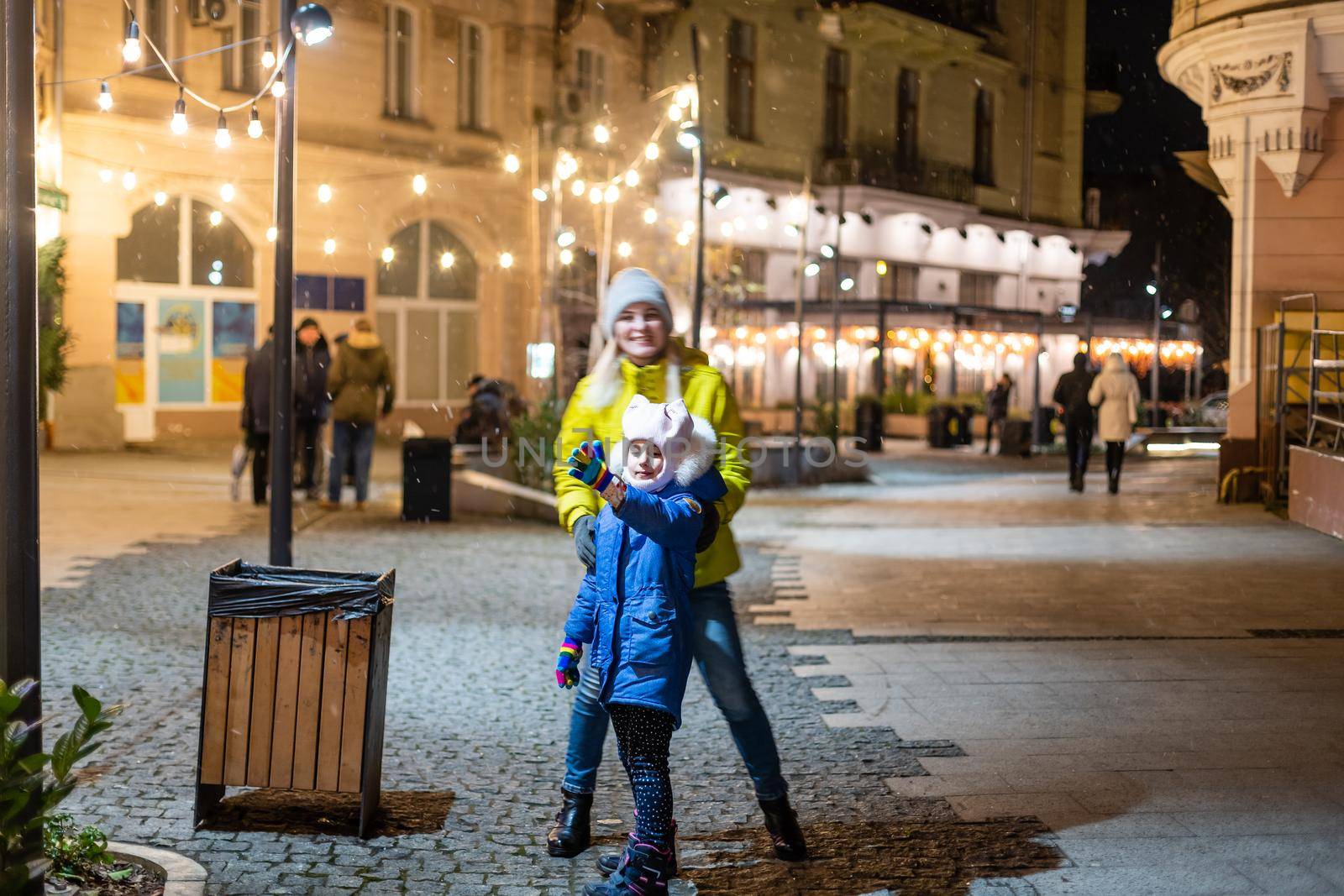 Mother with child girl at Christmas market celebrating New Year holiday. Family outdoor winter activity. Mom and daughter spend time together. Authentic lifestyle