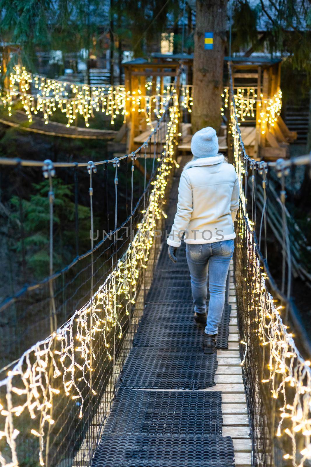 Winter lifestyle at Christmas. Caucasian woman on suspension bridge in garland Smiling with Christmas lights with a flaming torch and sparks by Andelov13