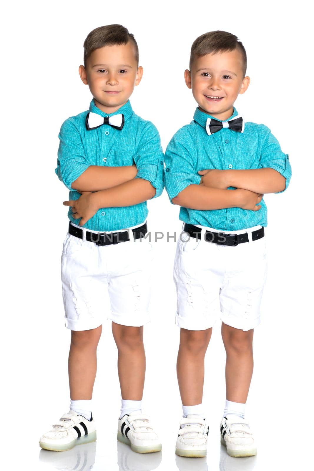 Two cute little boys stand in front of the camera in full growth. The concept of a happy childhood, the development of a child in the family. Isolated on white background.