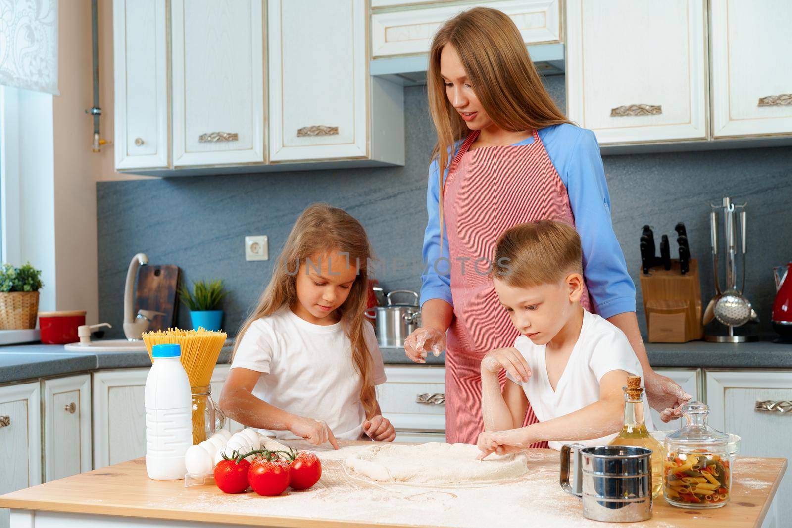 Young mother and her cute kids cooking pizza together in kitchen