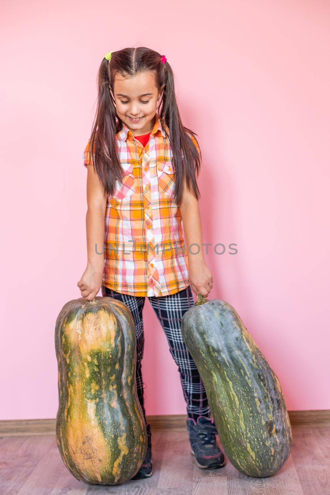 Picture of cheerful positive little girl with pumpkin over pink wall background holding pumpkin showing peace. by Andelov13