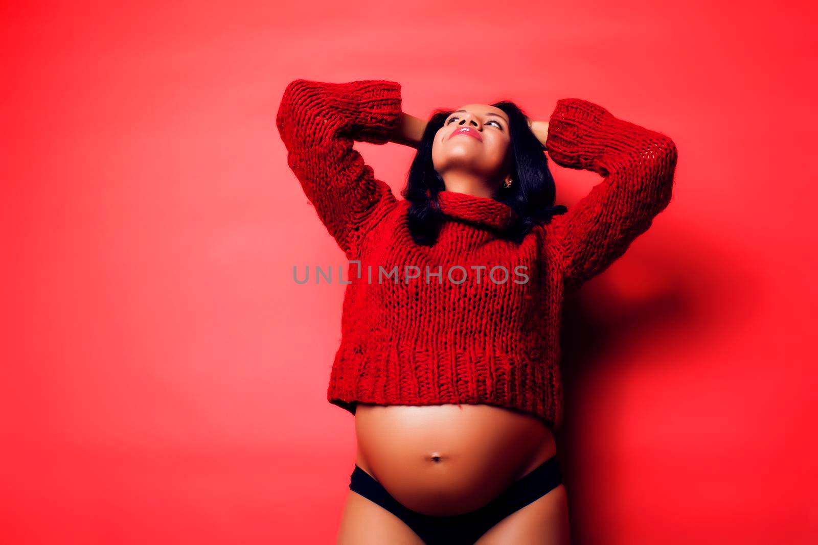 close up portrait of pregnant woman with big belly, hands hold, red sweater on background, choise of gender, lifestyle people concept