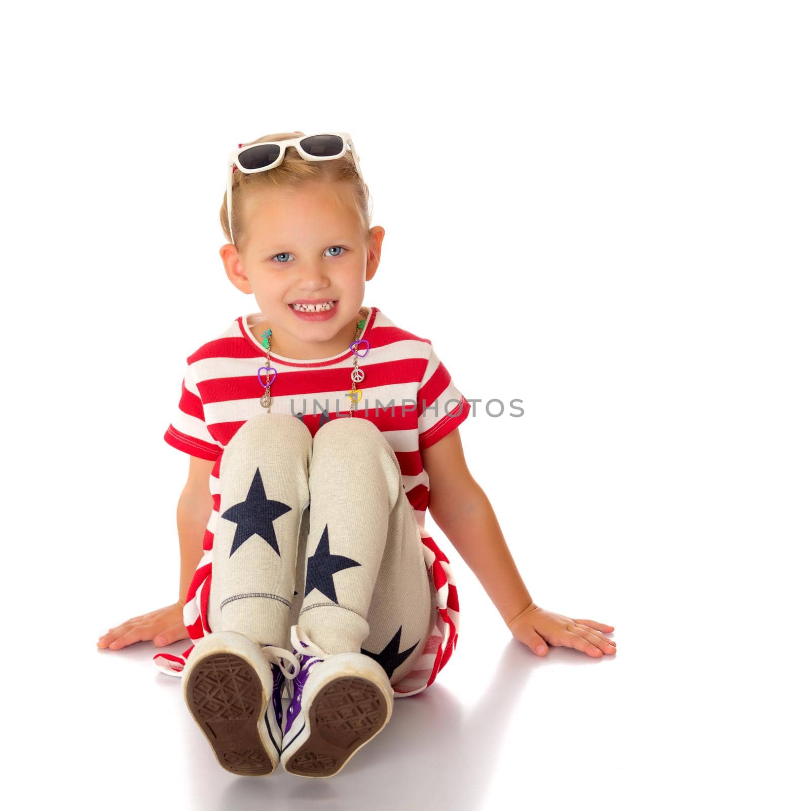 Beautiful little girl is sitting on the floor in the studio. The concept of a happy childhood, beauty and fashion. Isolated on white background.