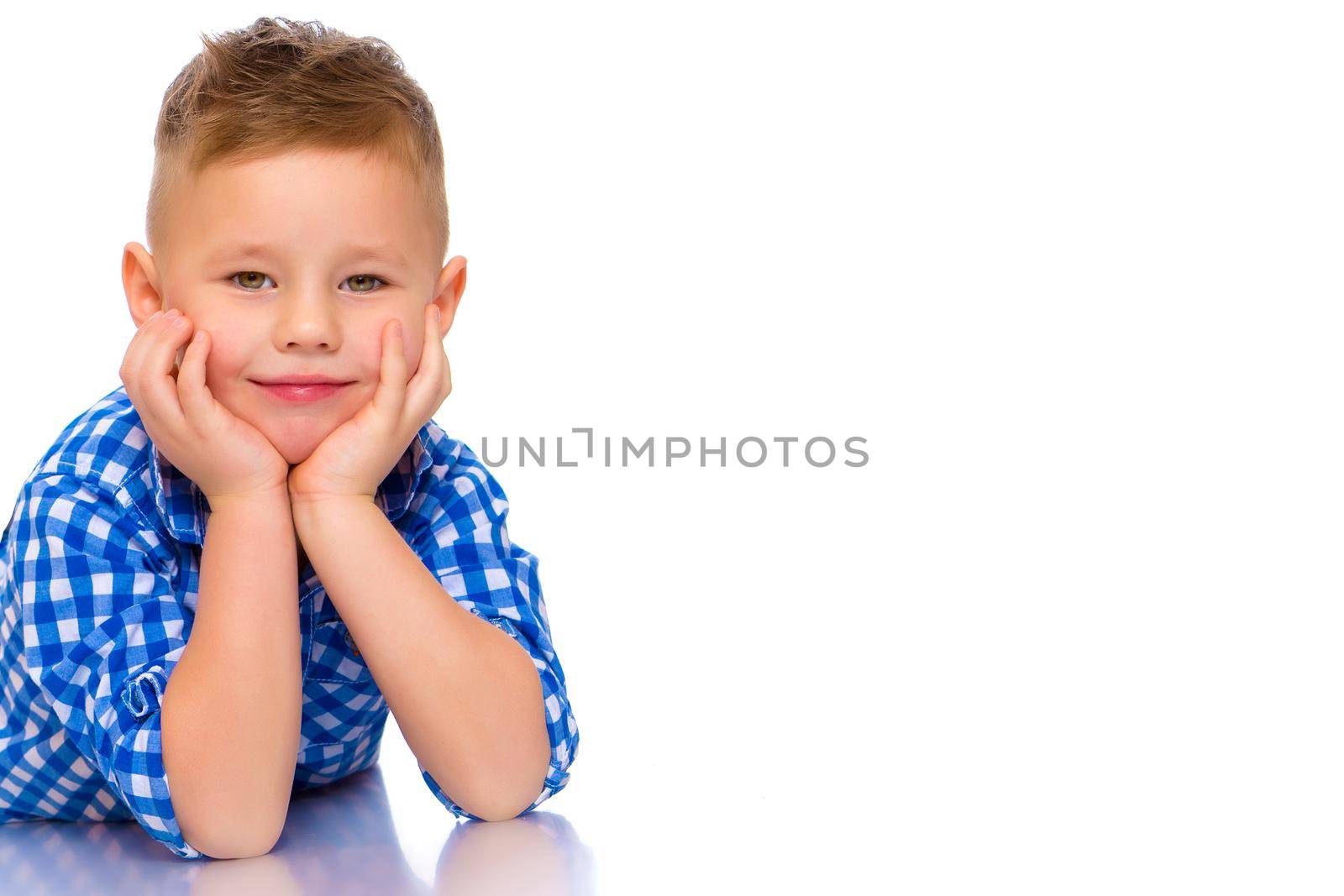 Happy little boy lies on the floor in the studio on a white background. The concept of a happy childhood, rest and vacation. Isolated.