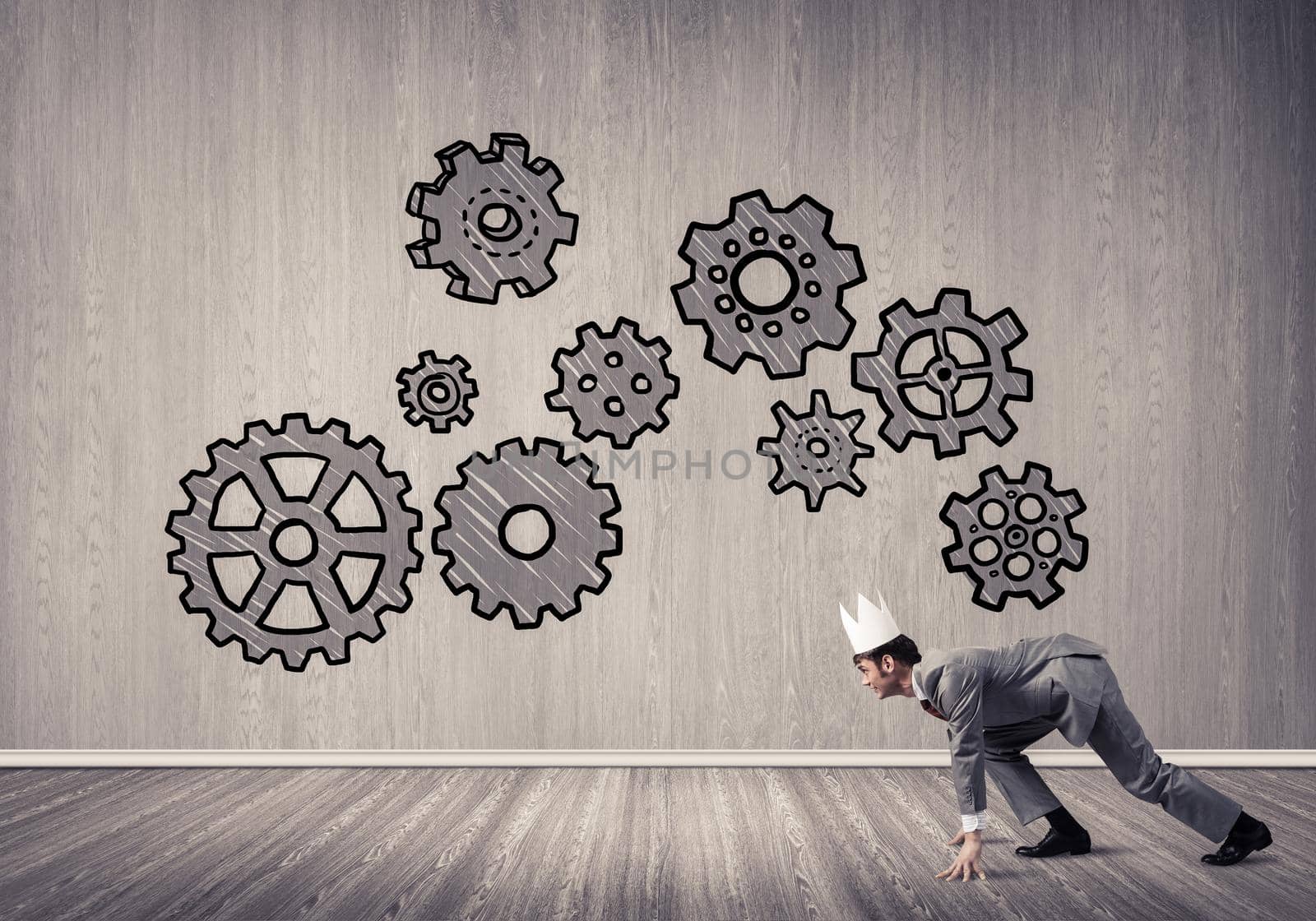 Young handsome businessman wearing white paper crown running and gear mechanism on wall