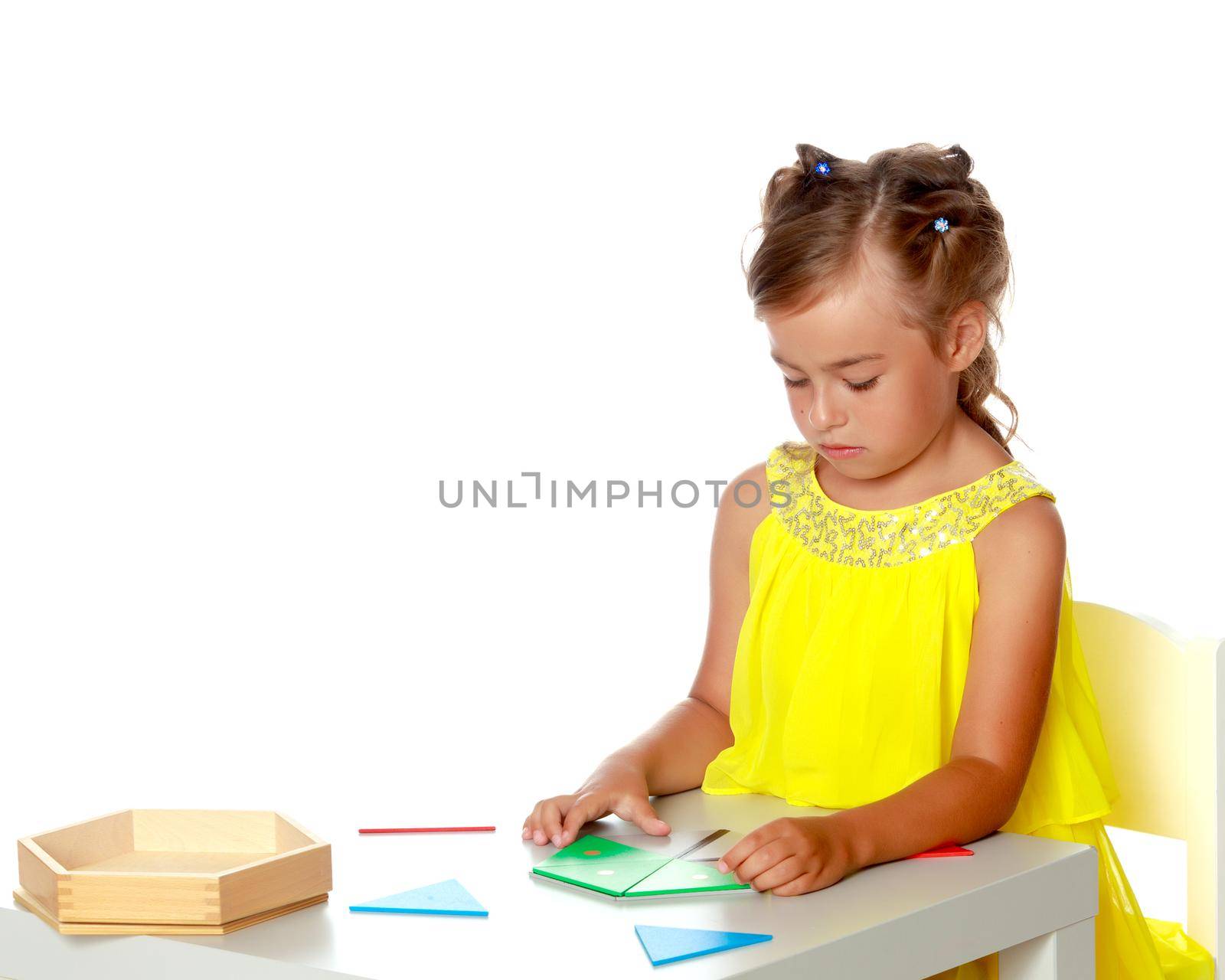 A little girl in Montessori kindergarten sits at a table and studies Montessori stuff. The concept of school and preschool education, harmonious development of the child. Isolated on white background.