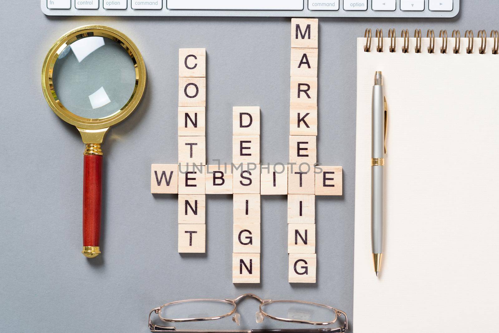 Web marketing concept with words from cubes. Still life of office workplace with crossword. Flat lay grey surface with pc keyboard and notebook. New strategy planning and workflow optimization.