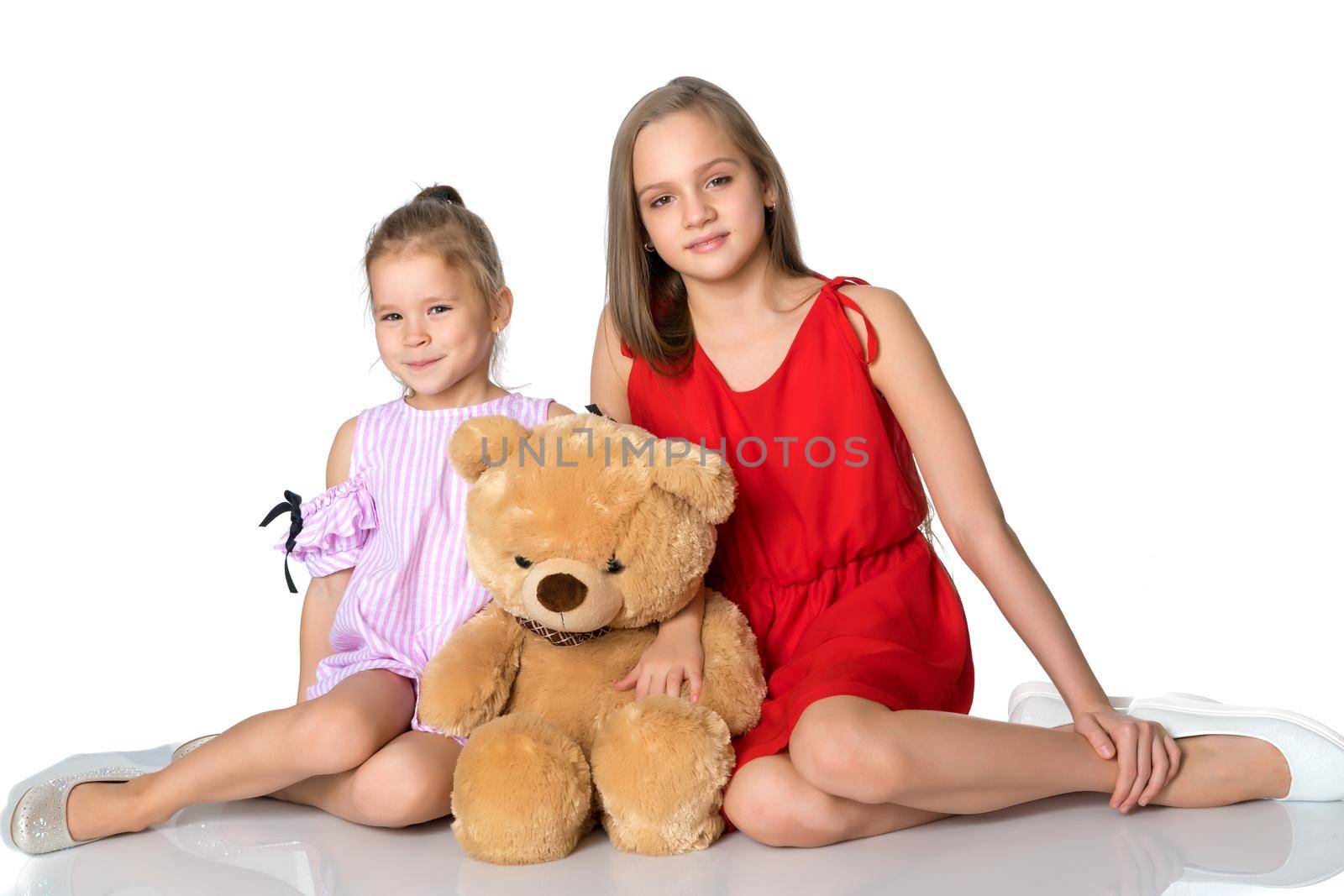 Lovely little girls. Next to a large teddy bear on a white background in the studio. The concept of holidays, happy childhood. Isolated.