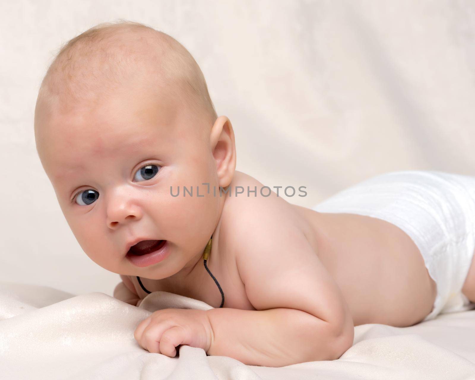 A charming baby lies on the blanket and looks into the camera. The concept of a happy childhood, the birth and upbringing of a child.
