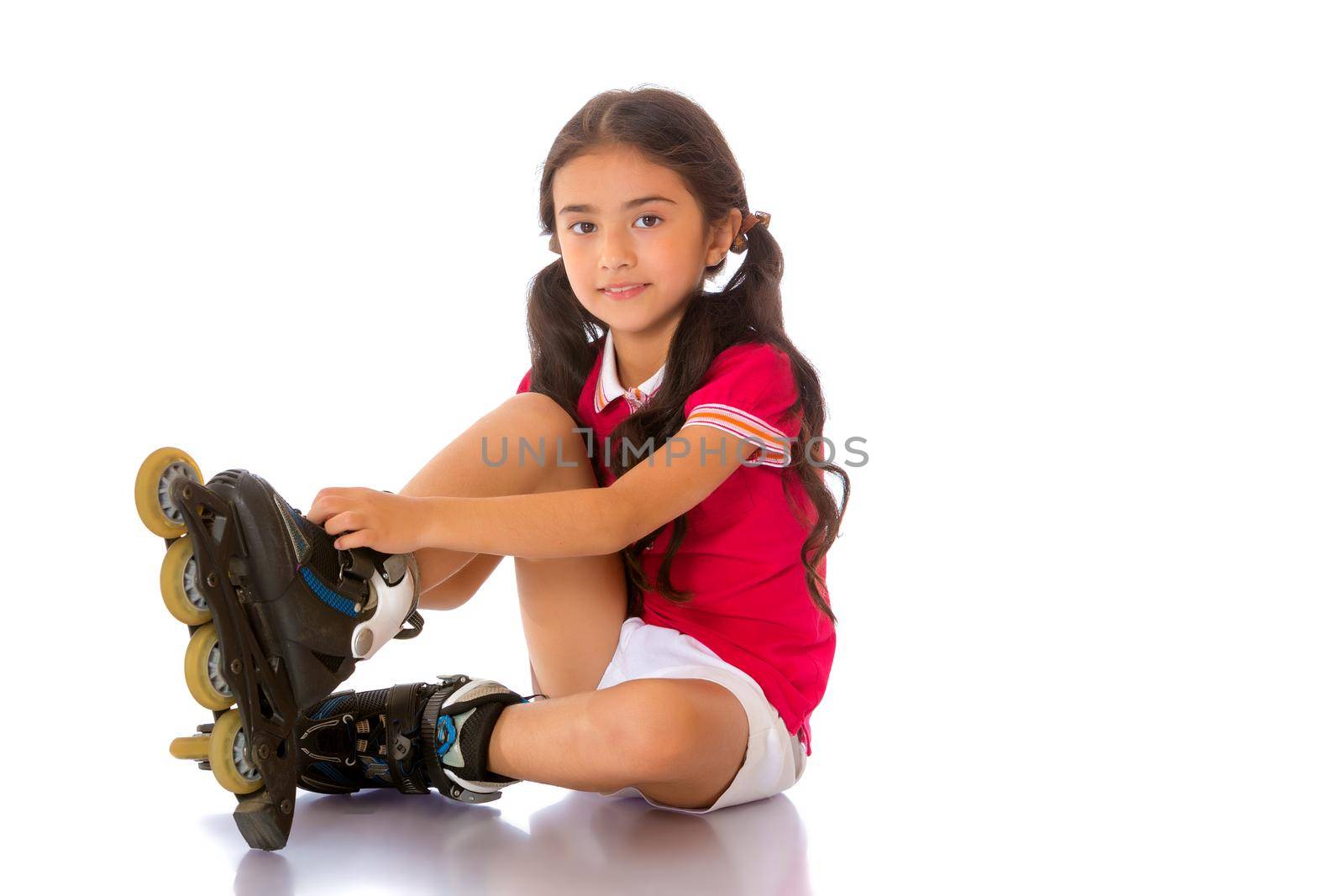 Beautiful little Asian girl puts on roller skates. The concept of advertising sports goods, a healthy lifestyle. Isolated on white background.