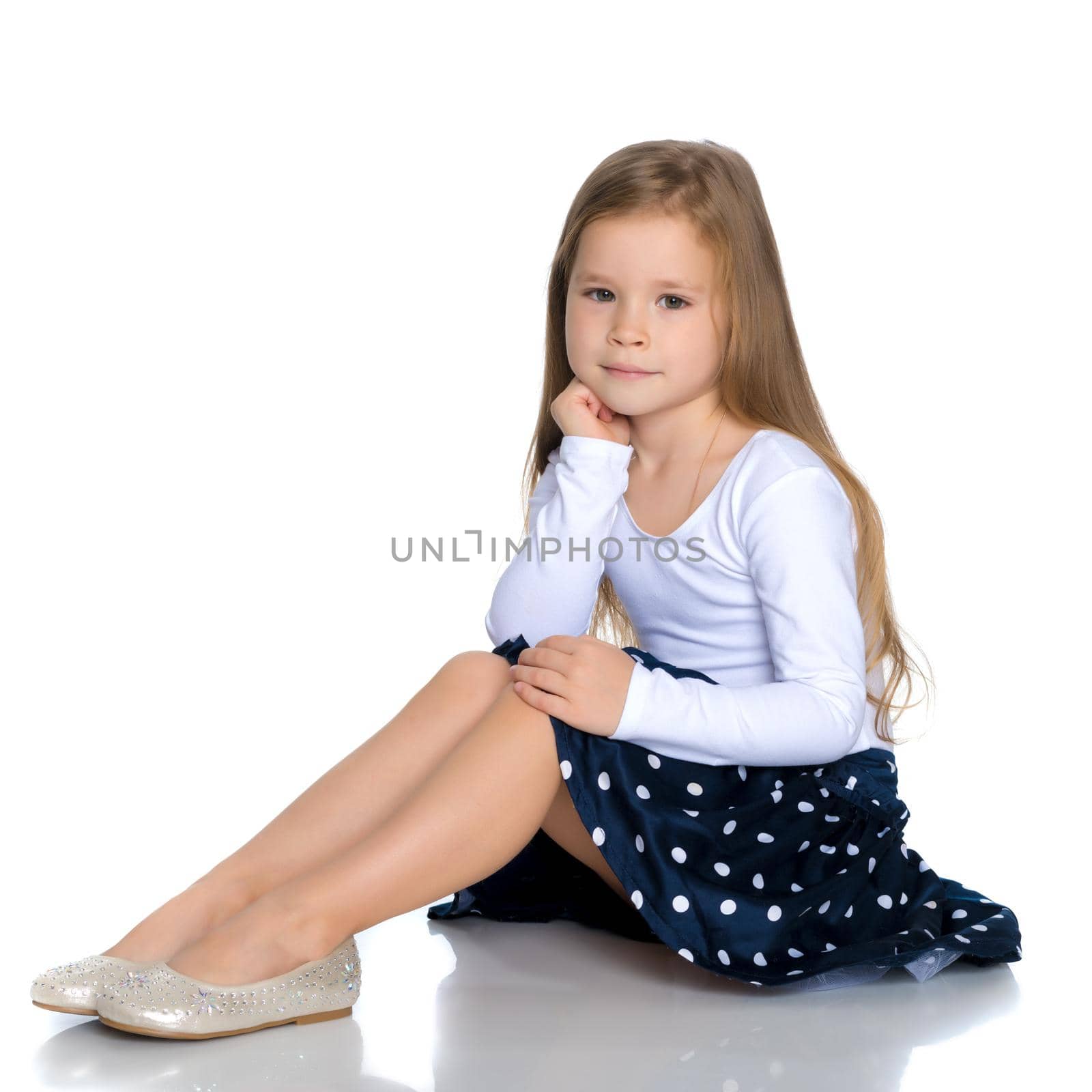 Beautiful little girl is sitting on the floor in the studio. The concept of a happy childhood, beauty and fashion. Isolated on white background.