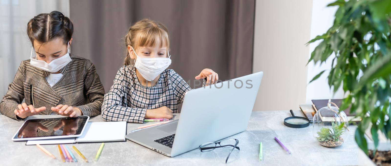 Distance Learning. School Girls At Laptop Wearing Mask Studying Online Sitting at the table at home by Andelov13